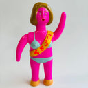 Toy figure of a character in a pink outfit with a colorful sash on a white background
