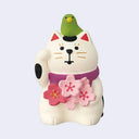 Small cat figurine with a bird on its head and cherry blossoms on a light purple background