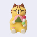Yellow cat-shaped figurine holding a stick of dango and a sakura mochi, sitting with a cherry blossom petal on its head and foot.