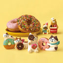 Series of several cat figures, eating donuts or hugging large donuts. In the background is a plate of real donuts.