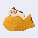 Magnet shaped and designed as a small cat laying atop of a very large fish shaped pastry (taiyaki).