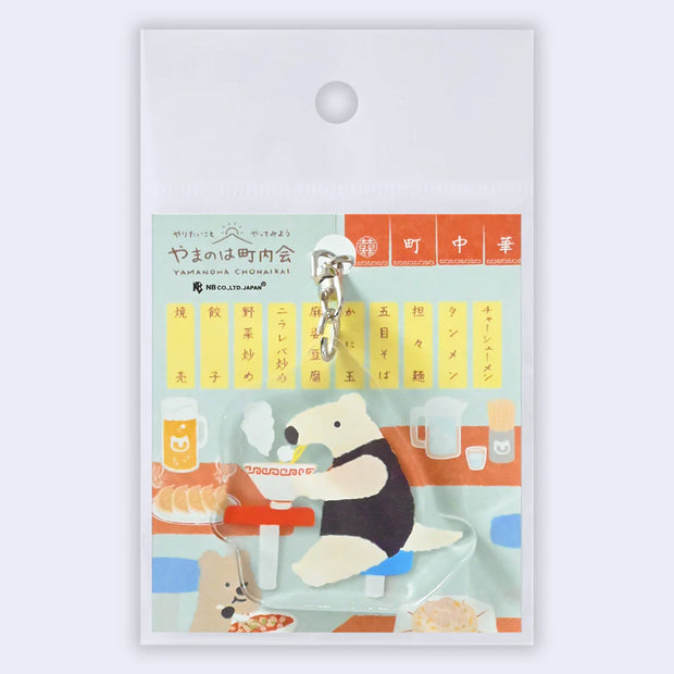 Acrylic keychain of an anteater sitting at a stool and eating a steaming bowl of noodles.
