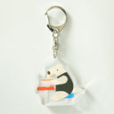 Acrylic keychain of an anteater sitting at a stool and eating a steaming bowl of noodles.