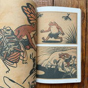 Open book with traditional Japanese frog illustrations on a wooden surface