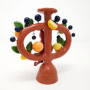 Ceramic sculpture designed as a Mexican tree of life sculpture, a brown 2 handled vessel with a red devil on the front. Around the handles are lemons, limes and oranges with leaves. Hanging off and protruding out via wire are decorative black balls.