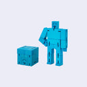 Wooden robot made out of many rectangular parts standing with its arms on its hips. The same robot is folded into a perfect cube shape in front.