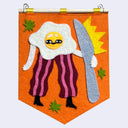 Felt banner, orange, with a design of an egg wearing striped pants and holding a butter knife as tall as itself.