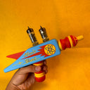 Wooden assembled toy gun with 'Atomic Blast' text and atom symbol on a yellow background