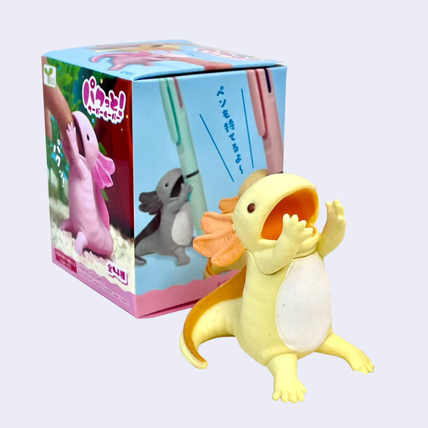 Small figurine of a yellow axolotl, sitting with its hands in front of its open mouth, with space in between to hold a pen.