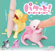 4 axolotl figurings, sitting with their hands in front of their open mouth, with space in between to hold a pen. Color options are: yellow, pink, purple and gray.