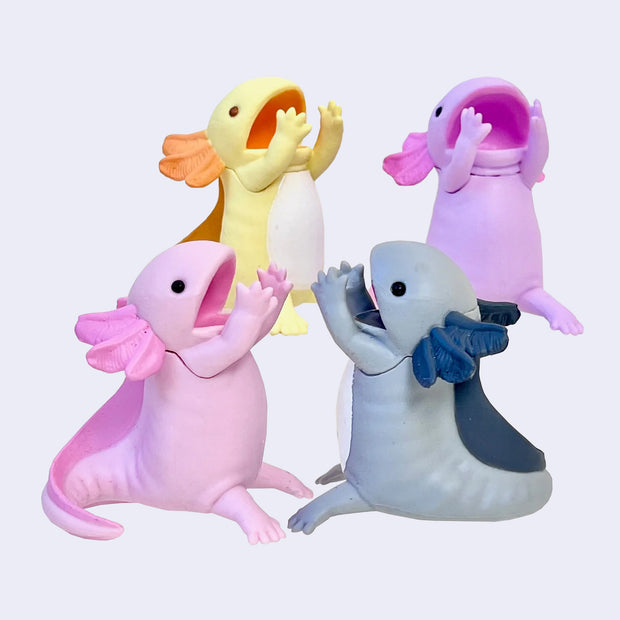 4 axolotl figurings, sitting with their hands in front of their open mouth, with space in between to hold a pen. Color options are: yellow, pink, purple and gray.