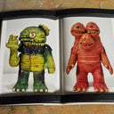 Two toy figures, one green and one orange, displayed in an open book against a textured background.