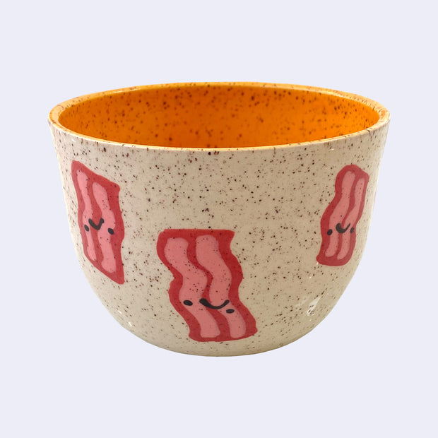 Ceramic bowl with spotted finishing and an earthy brown exterior and bright orange interior. On the outside are painted on cartoon style bacons, with simple expressions.