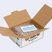 Open box of miniature stickers, made to resemble a shipping box with bubble wrap around the product and a small invoice. Exterior of box looks like realistic bakery bread box.