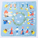 A square light blue fabric scarf featuring a colorful folk-art illustration of dancing figures, flowers, birds, and baskets arranged around a central wreath motif.