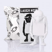 White figurine of a monkey wearing a sign - with a black and white box labeled 'Laugh Now' on a light gray background