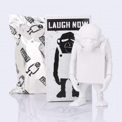 White figurine of a monkey wearing a sign - with a black and white box labeled 'Laugh Now' on a light gray background