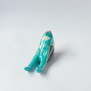Glossy, painted ceramic sculpture of a barn swallow bird, sitting with its turquoise and black wings at its side. It has a yellow stomach and black and red face with a yellow beak.