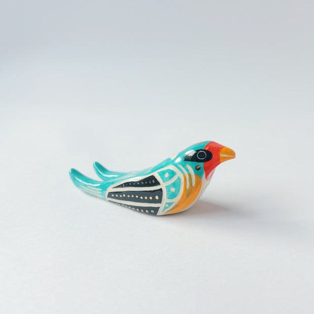 Glossy, painted ceramic sculpture of a barn swallow bird, sitting with its turquoise and black wings at its side. It has a yellow stomach and black and red face with a yellow beak.