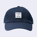 Navy blue cap with a small sewn on patch with foreign writing and a line art illustration of a cartoon dog wearing a pointy hat.