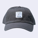 Gray cap with a small sewn on patch with foreign writing and a line art illustration of a cartoon dog wearing a pointy hat.