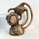 Ceramic figure with a rough cream and brown colored finishing of a character dressed like a monkey, positioned upside down over a rounded mound.