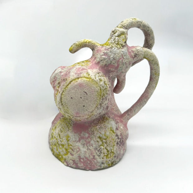 Ceramic figure with a rough cream colored, light pink and light green finishing of a character dressed like a monkey, positioned upside down over a rounded mound.