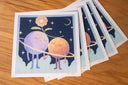 Stack of prints featuring an illlustration of 2 anthropomorphized moons, holding hands with a flower aboved their heads. They stand within a ring against a starry night sky