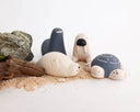 Wooden figure of a gray and white turtle with a rounded shell, flat belly and cute cartoon frown.