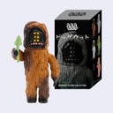 Toy figure of a character resembling Bigfoot with a box labeled 'Bigwoot Figure Collection' on a light gray background. It holds a skinny green mushroom and has 3 yellow eyes.