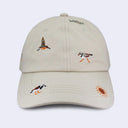 A light beige baseball cap featuring embroidered birds and a sun on the front panels and brim, set against a plain light gray background.