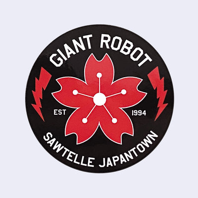 Black circle sticker with "Giant Robot" written on top in white font and "Sawtelle Japantown" written on bottom. A red cherry blossom is in middle with two red lightning bolds on each side.