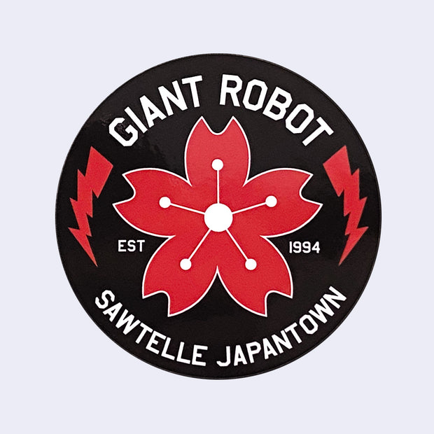 Black circle sticker with "Giant Robot" written on top in white font and "Sawtelle Japantown" written on bottom. A red cherry blossom is in middle with two red lightning bolds on each side.