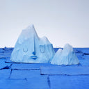 Set of 2 carved wooden sculptures, painting blue, of mountain ranges. One has a closed eye, calm facial expression and the other is without a face and smaller in size.