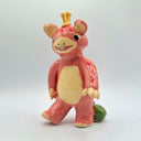 Glazed ceramic sculpture of a pink bear-like monster with cute, buck-teeth and a yellow crown of sorts. Its body has pink polka dots and it balances its tail on a small watermelon.