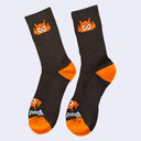 Dark brown socks with an orange cartoon robot head on them and orange colored heels and toes. The robot head decorates the cuff end of each sock so that it peeks out when you wear sneakers.