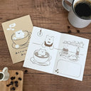 Illustrated card with a bear in a coffee cup on a wooden table with coffee beans and a mug.