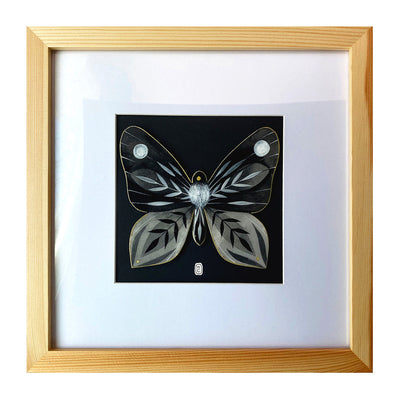 Illustration on cut out paper of a grey, black and white butterfly with abstract striped patterns on its wings, akin to leaves. Its body has white fur on it, like a moth. Piece if framed in light grain square wooden frame.