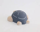 Wooden figure of a gray and white turtle with a rounded shell, flat belly and cute cartoon frown.