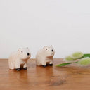 Two small capybara figurines on a wooden surface with a white background