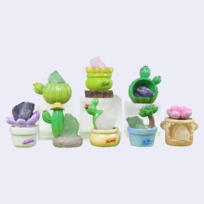 Set of colorful cactus-shaped figurines with various crystals on a light gray background