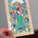 Postcard with a colorful illustration of a mouse holding a bird and standing amongst many flowers.