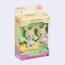 Two small rabbit dolls with cream colored flocked fur, dressed in small children's clothing. One pushes the other in a yellow car. In their product packaging.