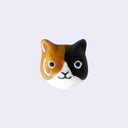 3D ceramic brooch/pin of a calico cat's head, with a simple and cute cartoon smile.