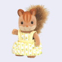 Small figurine of a squirrel, with flocked fur and a fluffy fabric tail. It wears a yellow dress with flowers on it.