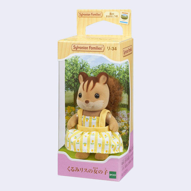 Small figurine of a squirrel, with flocked fur and a fluffy fabric tail. It wears a yellow dress with flowers on it. In its packaging box.