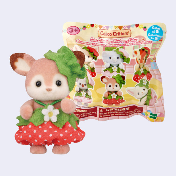 Small flocked deer figurine dressed in a strawberry dress and standing in front of its blind bag product packaging.