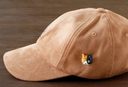 3D ceramic brooch/pin of a calico cat's head, with a simple and cute cartoon smile. Shown on a brown cap.
