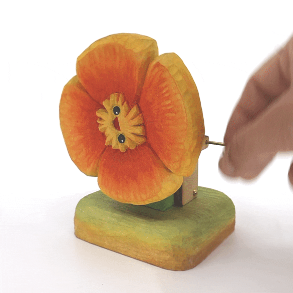 Gif of a wooden sculpture of a orange poppy with a small cartoonish face. Sculpture is on a stand and has a lever, rotating the face around like a clock.