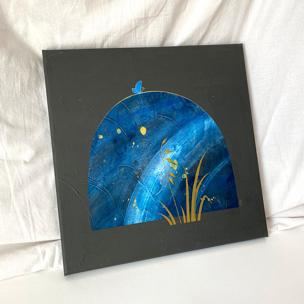 Collage style painting on dark gray canvas of a large rounded top rock, blue with white marbling and gold splatters. A small blue butterfly sits atop the rock and some blades of grass are in front. Displayed at an angle.